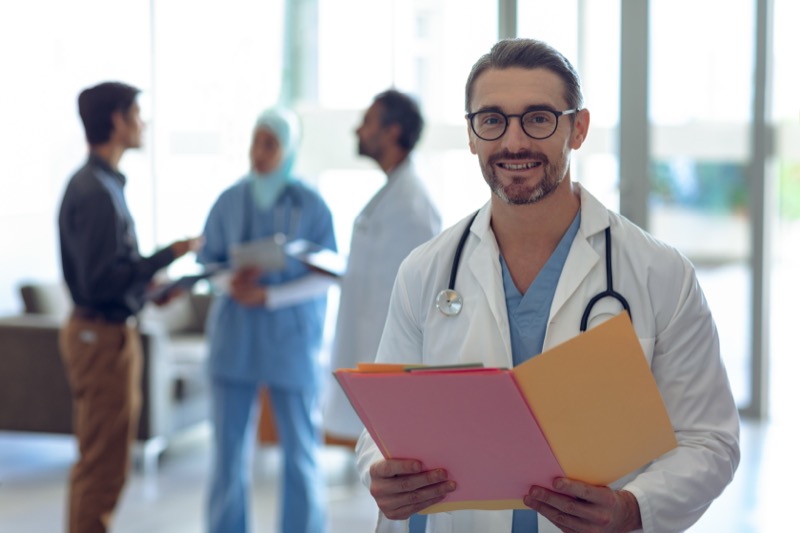 Doctor holding medical files with team in hospital background